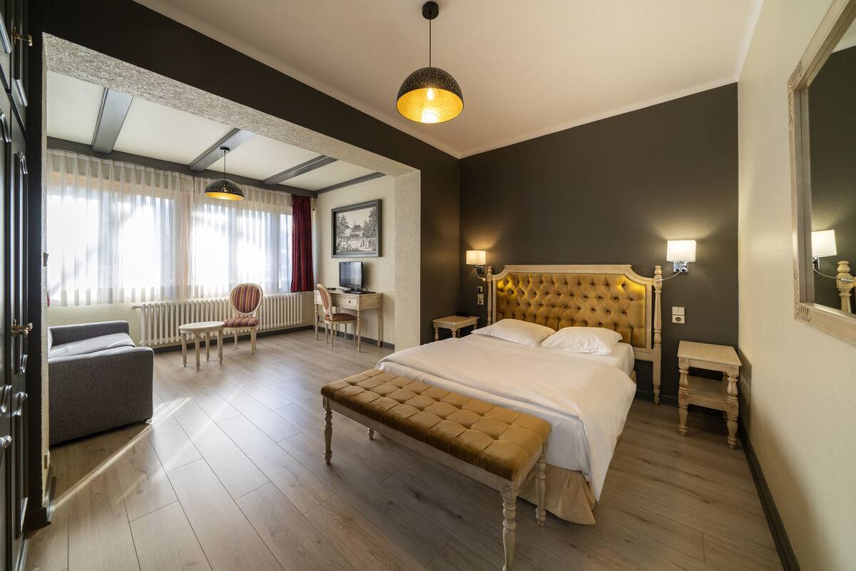 A hotel room with a large bed, a bench, a desk, and a chair.