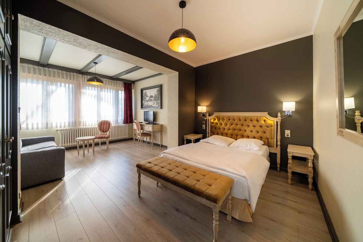 A hotel room with a large bed, a bench, a desk, and a chair.