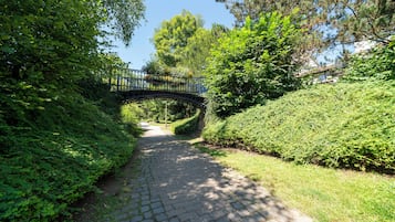 Un sentier pavé de pierres mène à travers un parc, et un pont métallique enjambe ce sentier.