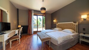Habitación de hotel con una cama grande, un escritorio con silla, televisión y balcón con cortinas.