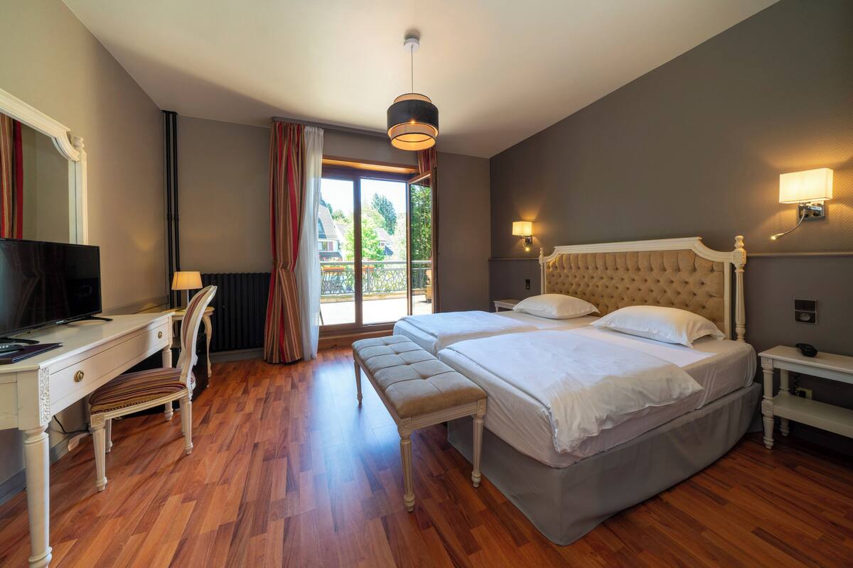 A bedroom with a double bed, a desk with a chair, a television, and a window with curtains.