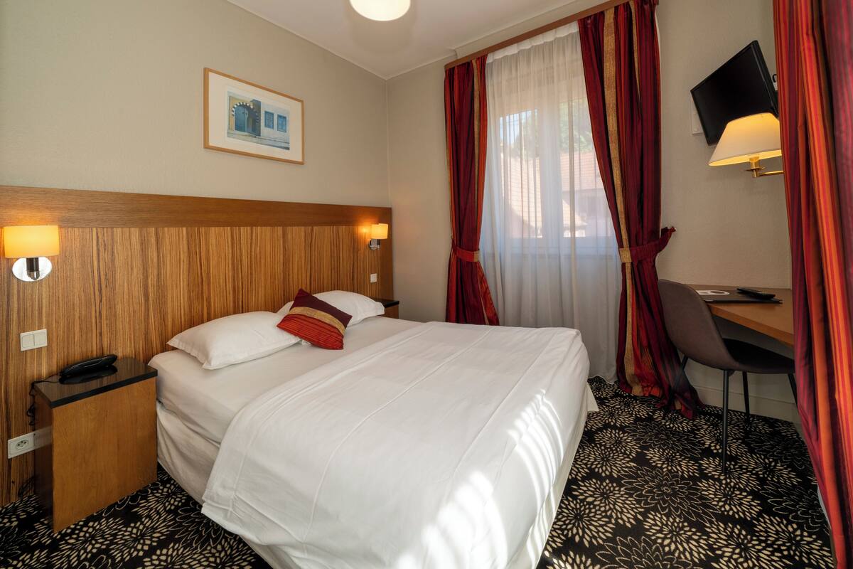 A hotel room with a bed, bedside lamps, a desk, and a television.