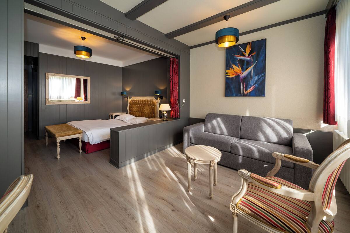 A modern hotel room with a bed, a sofa, a chair, and a dining table.