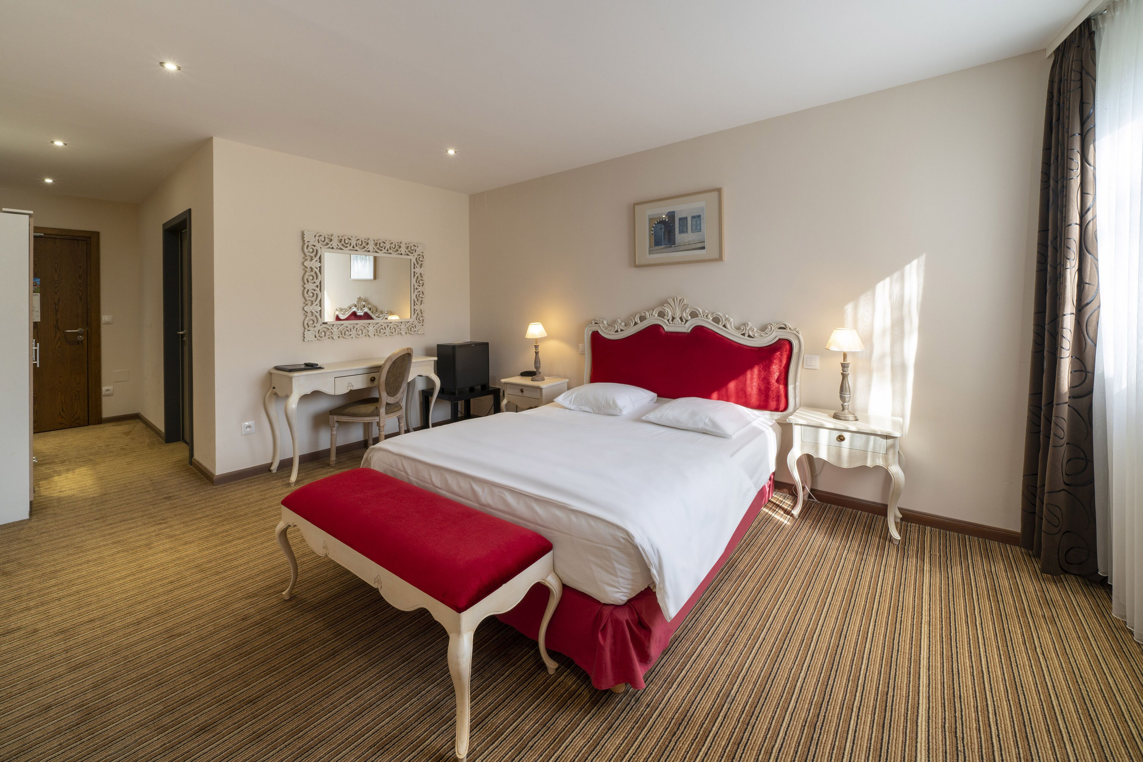 Habitación de hotel con una cama grande, un escritorio, una silla, un espejo y una ventana con cortinas.