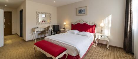 Habitación de hotel con una cama grande, un escritorio, una silla, un espejo y una ventana con cortinas.