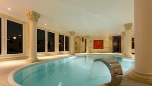 Una piscina interior con tobogán de agua, rodeada de columnas y grandes ventanales.