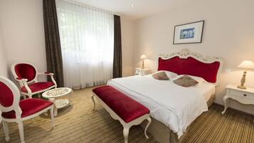Ein Hotelzimmer mit einem großen Bett, zwei Nachttischen, einer roten Bank, zwei roten Sesseln und einem kleinen runden Tisch.