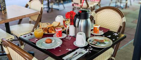A breakfast table set with bread, croissants, orange juice, a coffee pot, and a glass of wine.