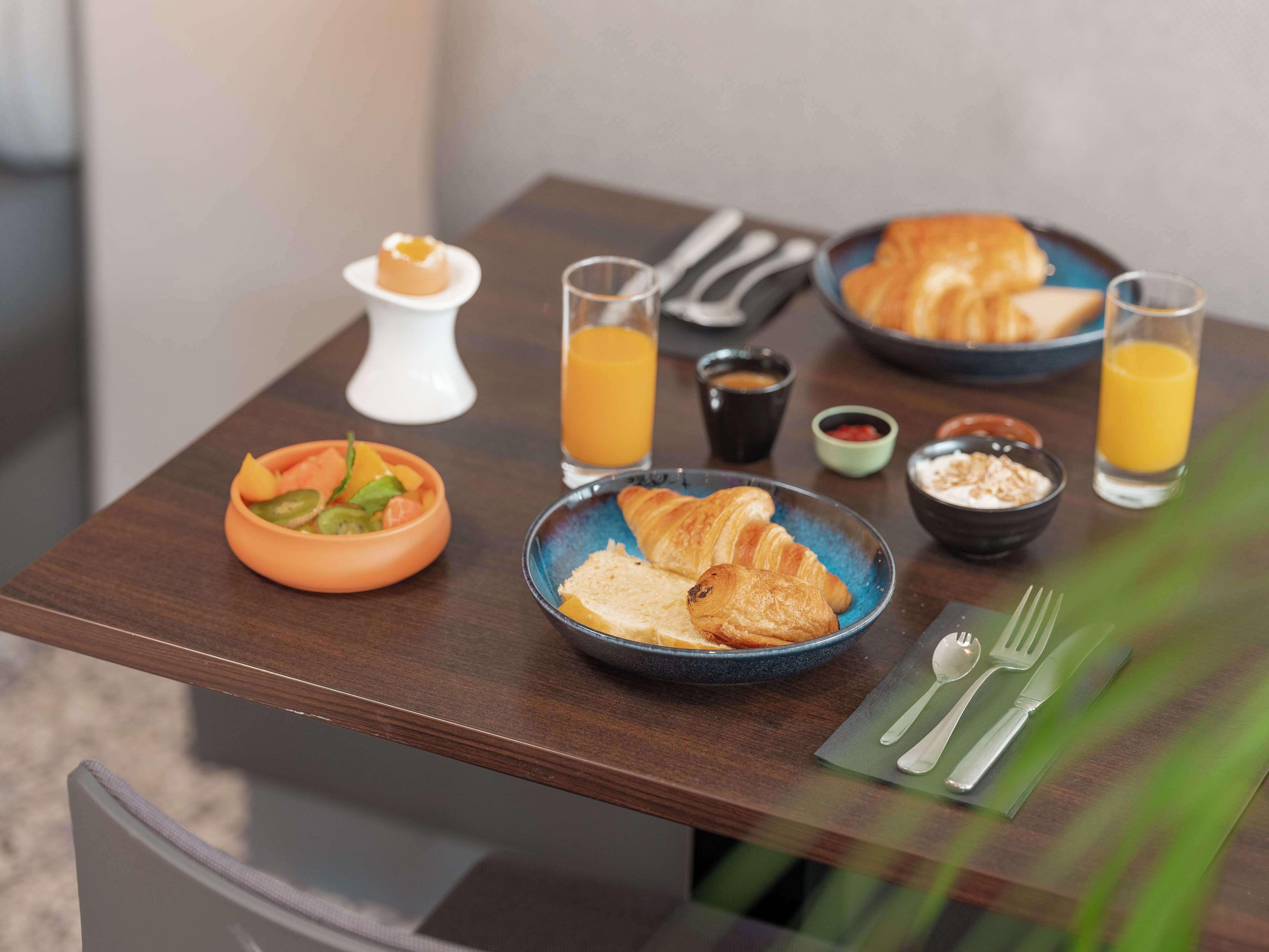 A breakfast table with croissants, fruit, and beverages.