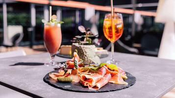 A table with a charcuterie board, a Bloody Mary, and a cocktail with a straw.