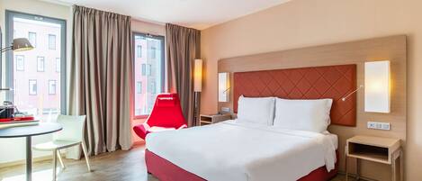 A hotel room with a large bed, a desk, a chair, and a view of the city.