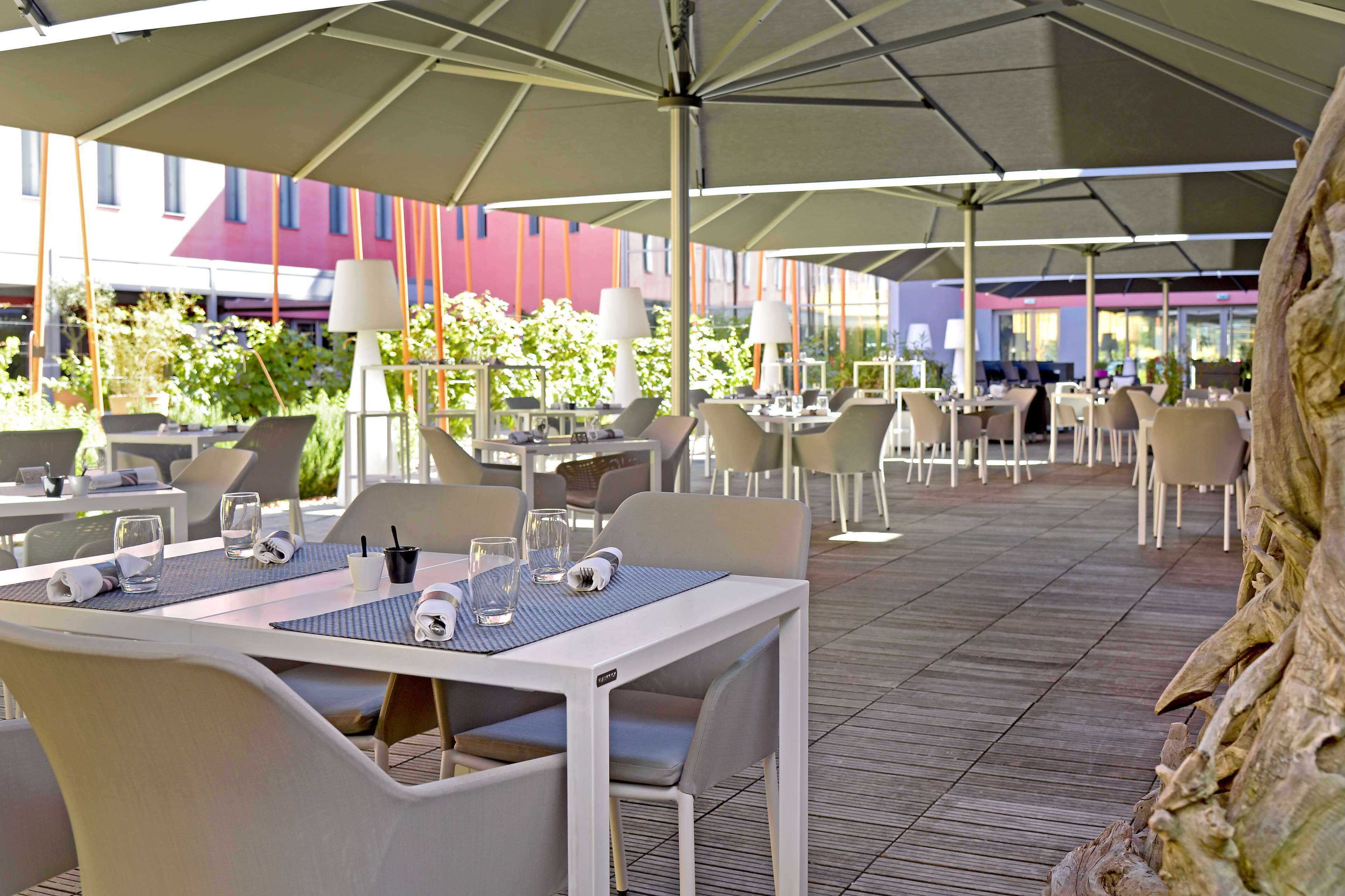 An outdoor dining area with tables and chairs, umbrellas, and a view of buildings in the background.