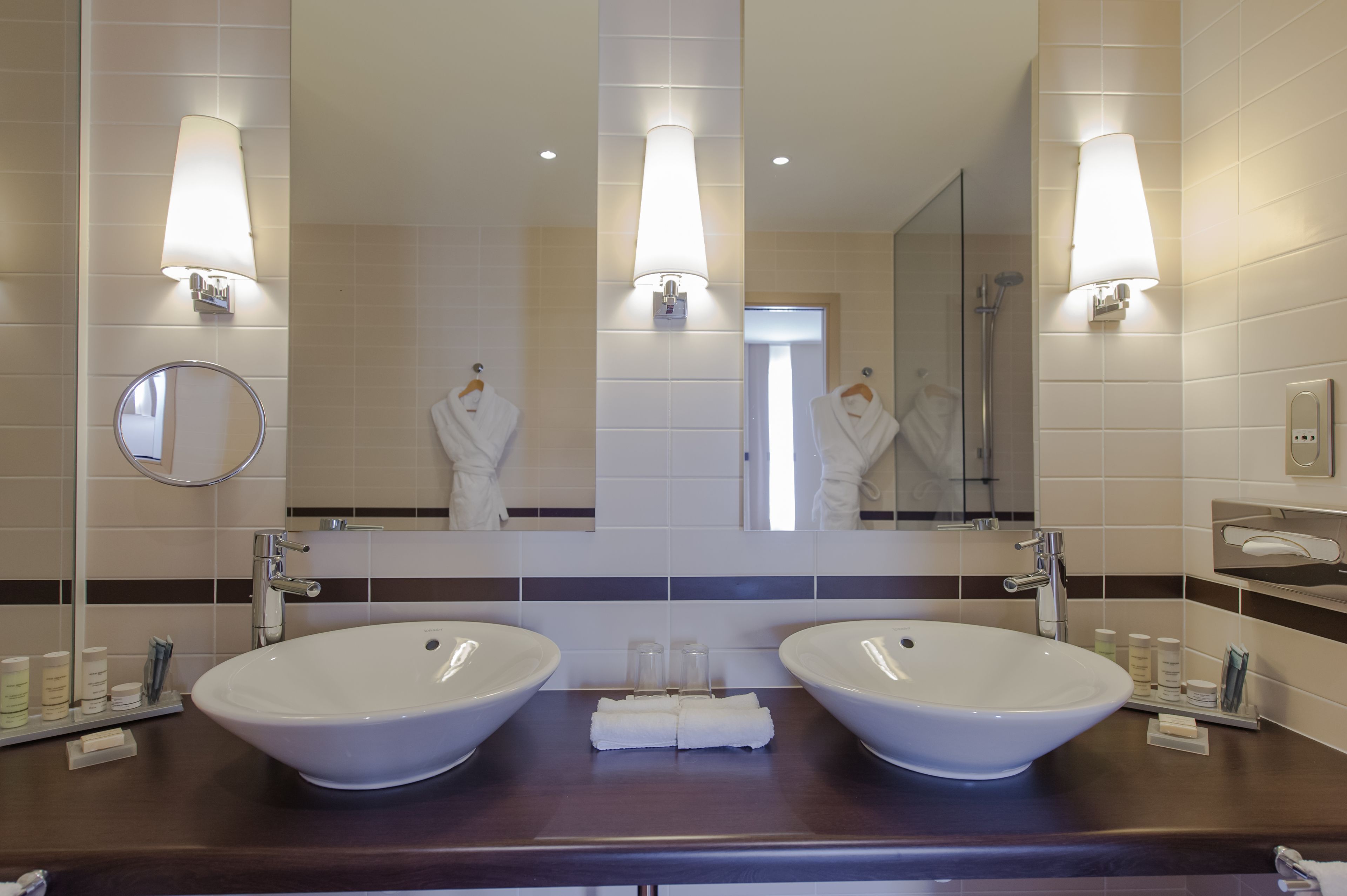 Ein Badezimmer mit zwei großen weißen Waschbecken, einem runden Spiegel und Wandleuchten.