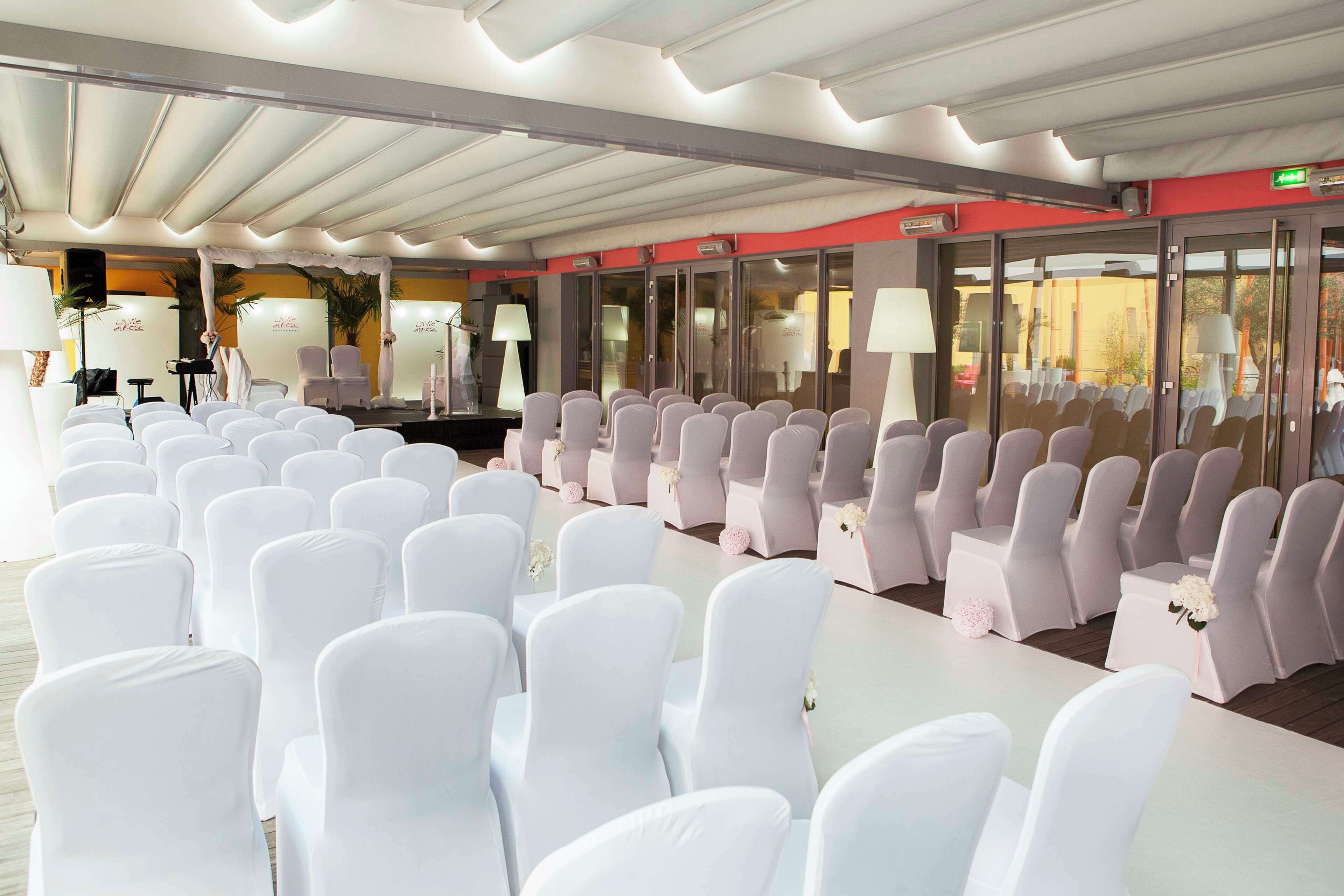 Een congreszaal met rijen witte stoelen, een podium met een piano, en een glazen wand met uitzicht.