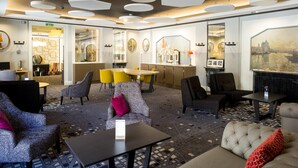 Un vestíbulo de hotel con una zona de comedor central, diversas opciones de asiento y un cuadro grande en la pared.