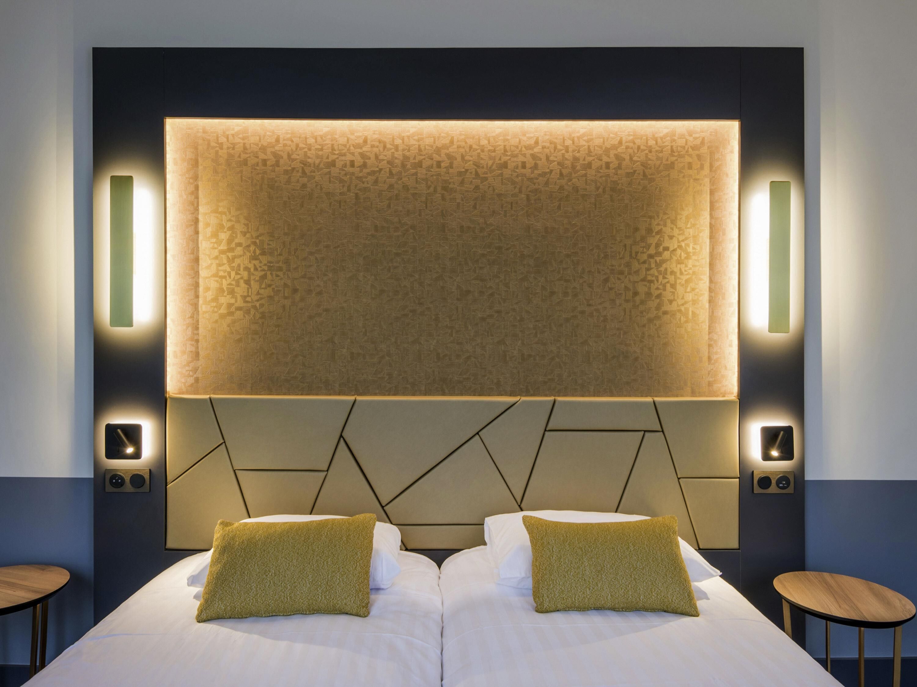 Een hotelkamer met een groot bed, twee nachtkastjes, een hoofdbord met geometrische patronen en wandlampen.
