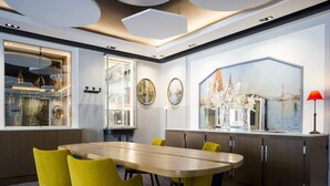 Un comedor moderno con una mesa larga, sillas amarillas, una vitrina de vidrio con botellas y un cuadro de un paisaje urbano.