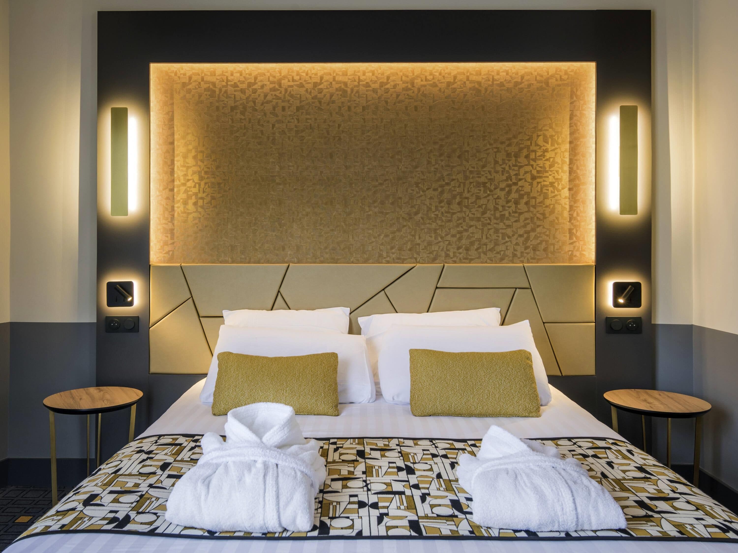 Ein Hotelzimmer mit einem großen Bett, zwei Nachttischen, einem Kopfteil mit integrierter Beleuchtung und einer gemusterten Tagesdecke.