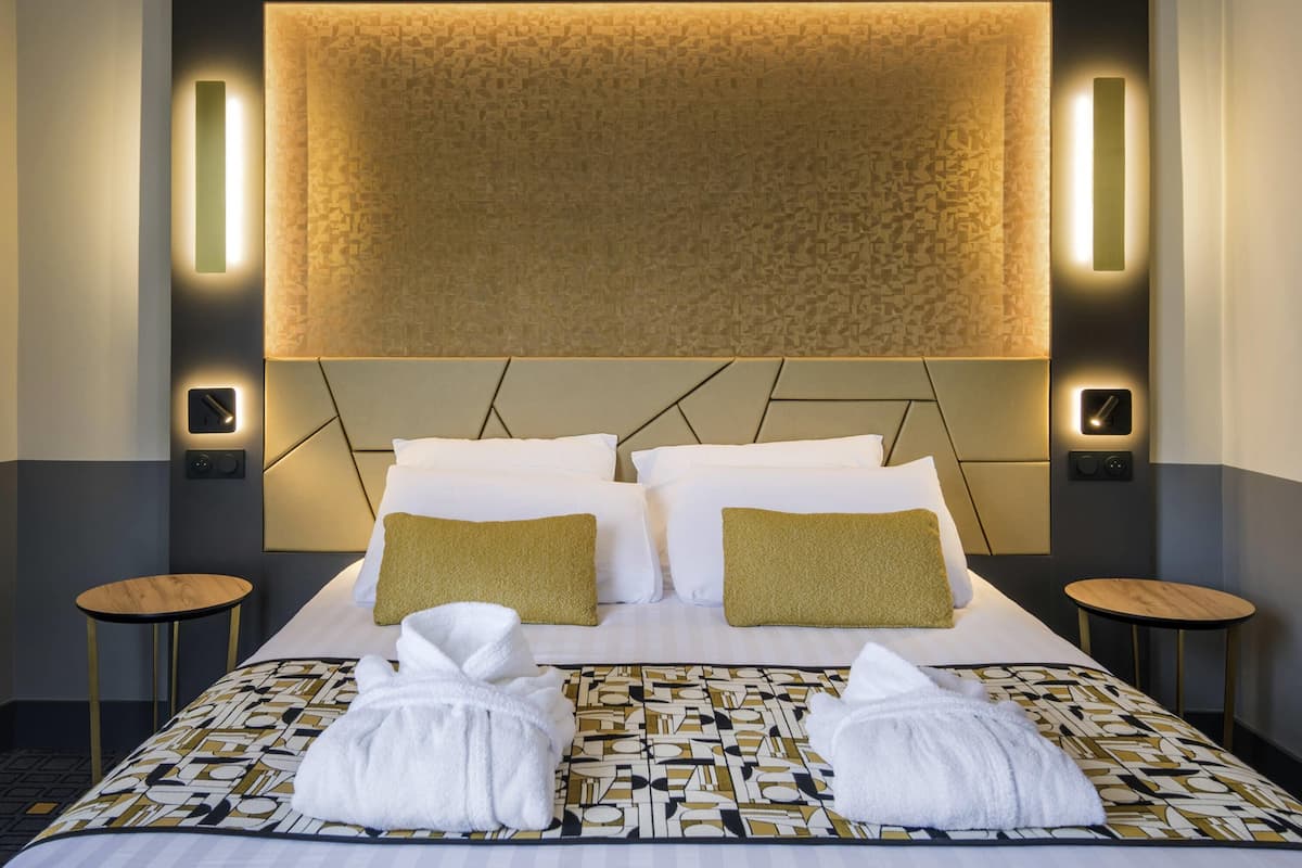 A hotel room with a large bed, two bedside tables, a headboard with integrated lighting, and a patterned bedspread.