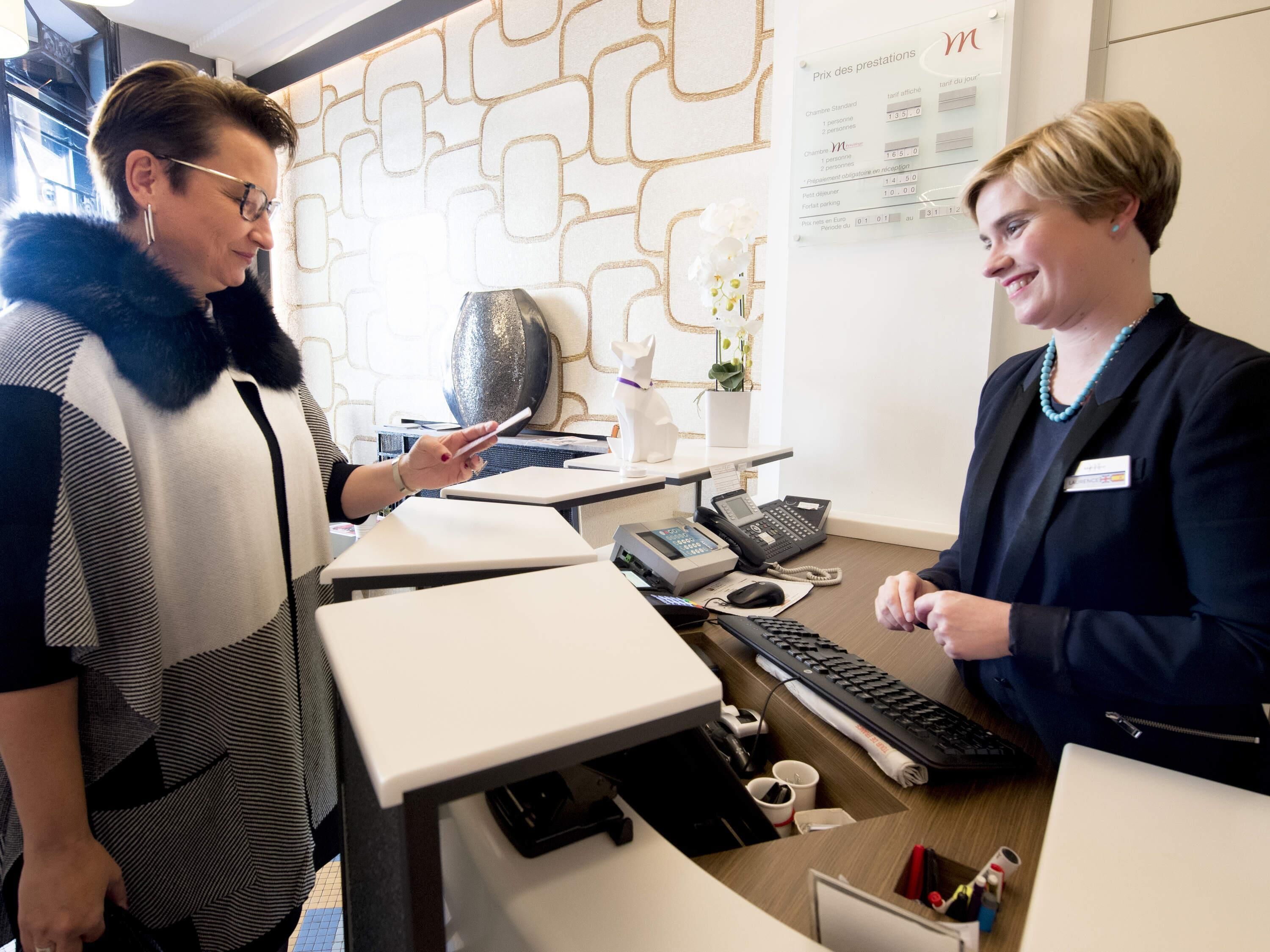 A reception desk with a name tag, a phone, a keyboard, and a small potted plant.