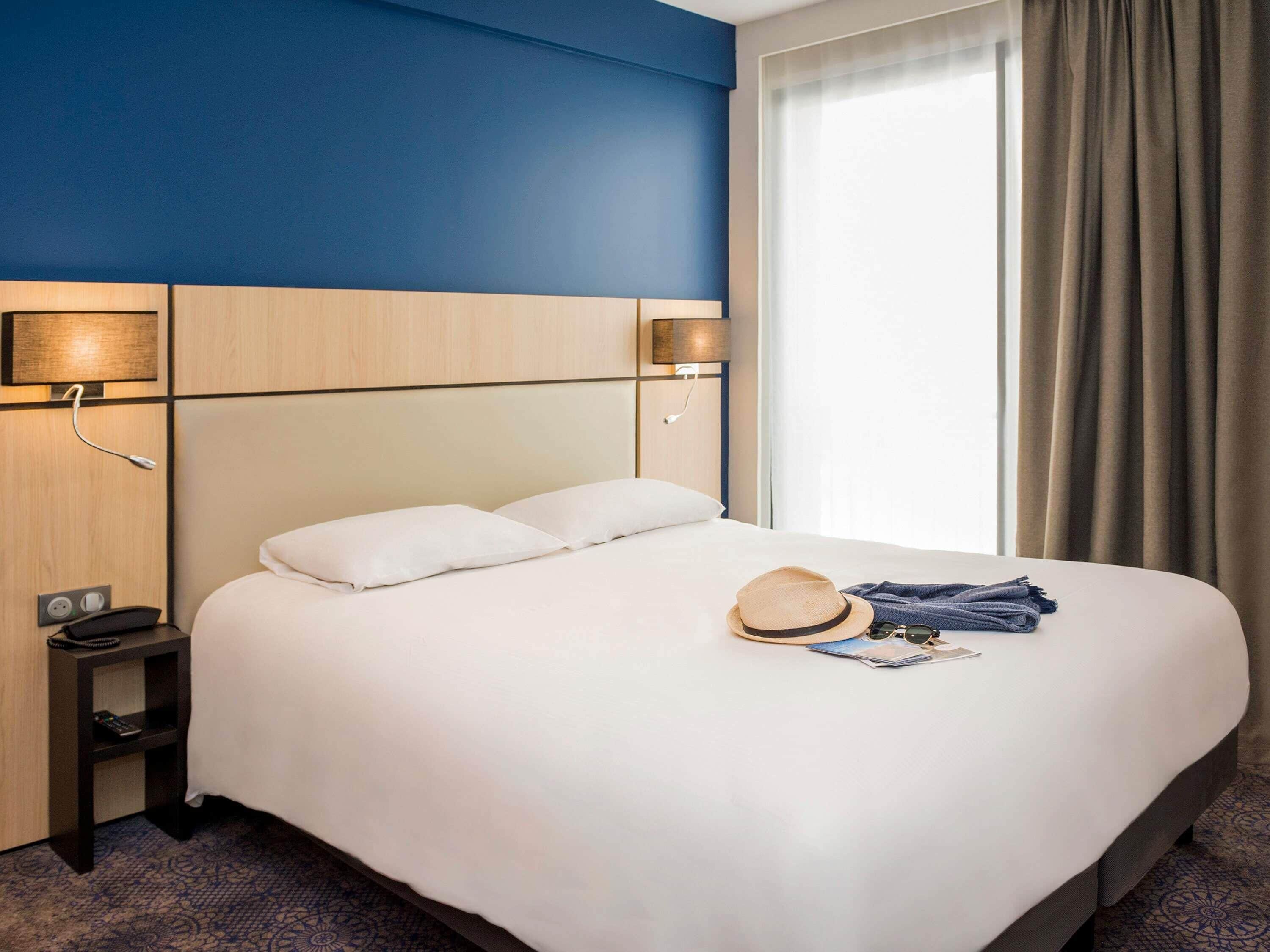 A hotel room with a bed, bedside lamps, a nightstand, and a window with curtains.