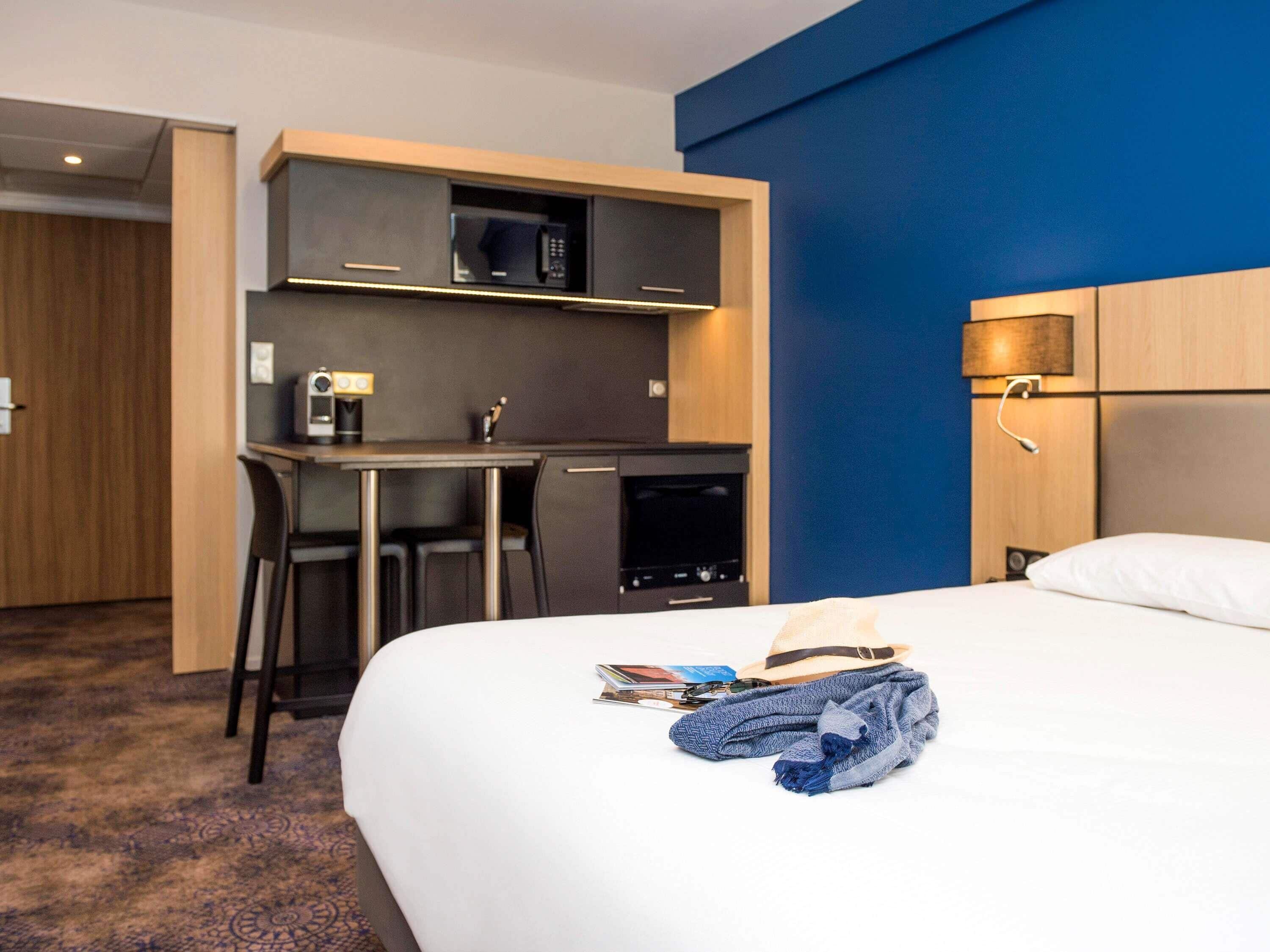 Habitación de hotel con cama, escritorio, computadora, microondas y cafetera.