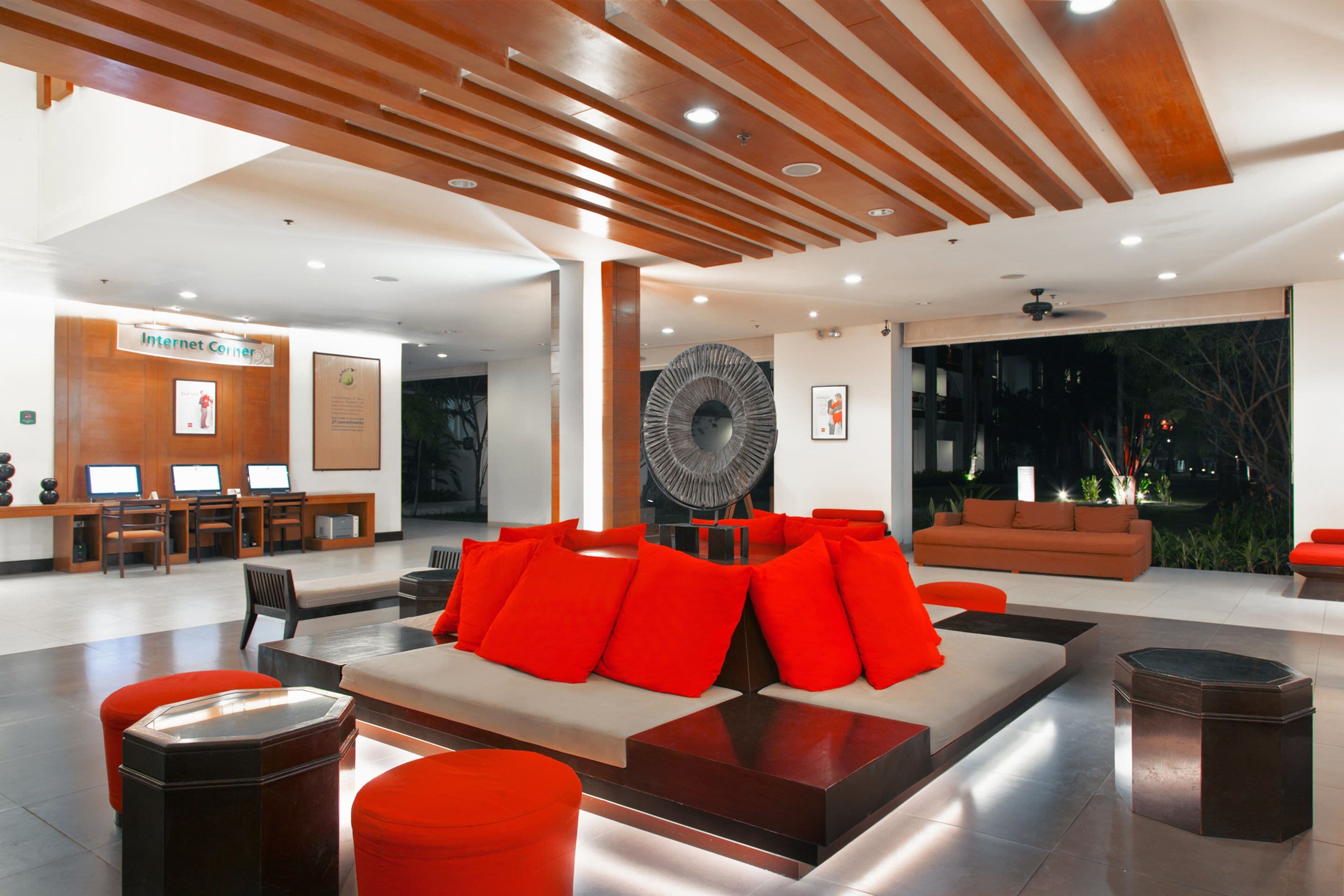 A modern lobby with a seating area featuring a sofa and ottomans, a reception desk, and a large fan.