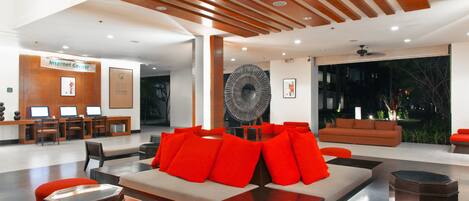 A modern lobby with a seating area featuring a sofa and ottomans, a reception desk, and a large fan.