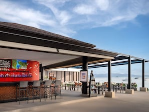An outdoor seating area with a bar, tables, chairs, and a view of the sea. - ibis Samui Bophut (Koh Samui)