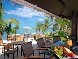 An outdoor seating area with tables and chairs, overlooking a body of water with boats, surrounded by palm trees. - ibis Samui Bophut (Koh Samui)