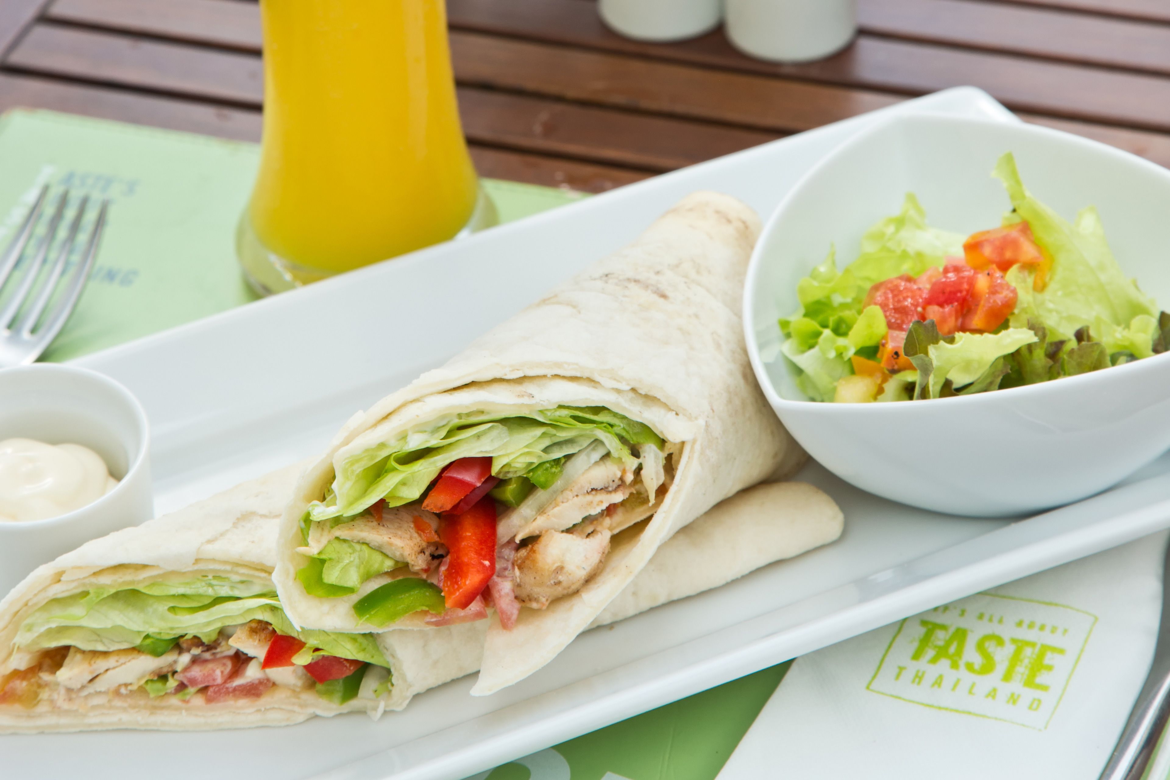 Un plato con un wrap, un bol de ensalada, una botella de jugo y una servilleta con un logotipo.