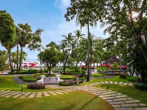 A landscaped garden with palm trees, a paved walkway, and outdoor seating areas. - ibis Samui Bophut (Koh Samui)