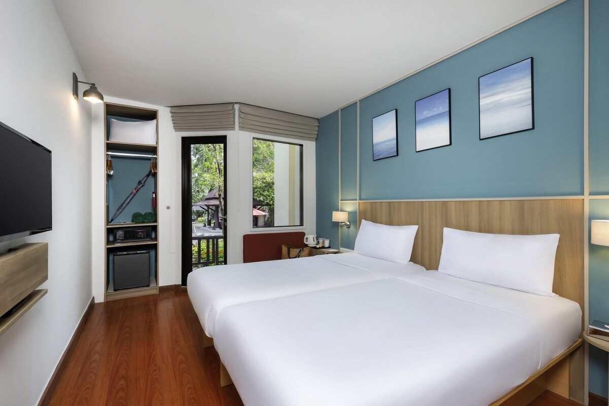 Habitación de hotel con una cama grande, televisión, escritorio con lámpara y vistas al exterior.
