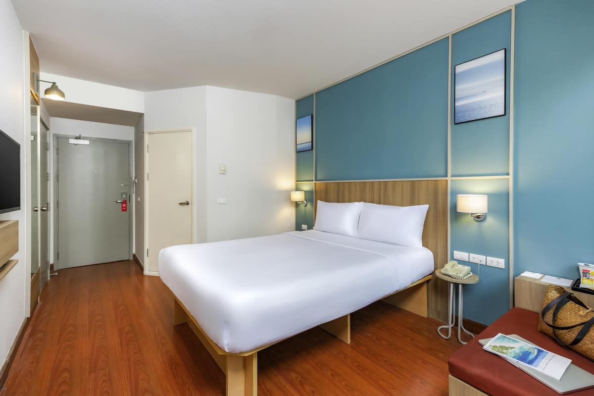 A hotel room with a bed, bedside lamps, a desk with a phone, a chair, and a wall-mounted TV.