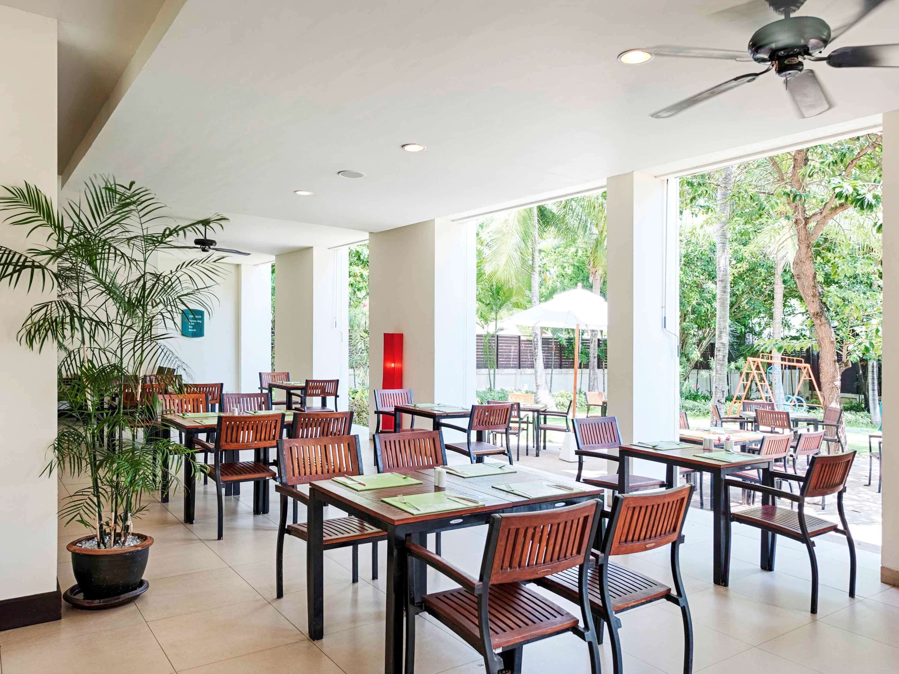 A spacious indoor dining area with multiple tables and chairs, large windows, and a ceiling fan.