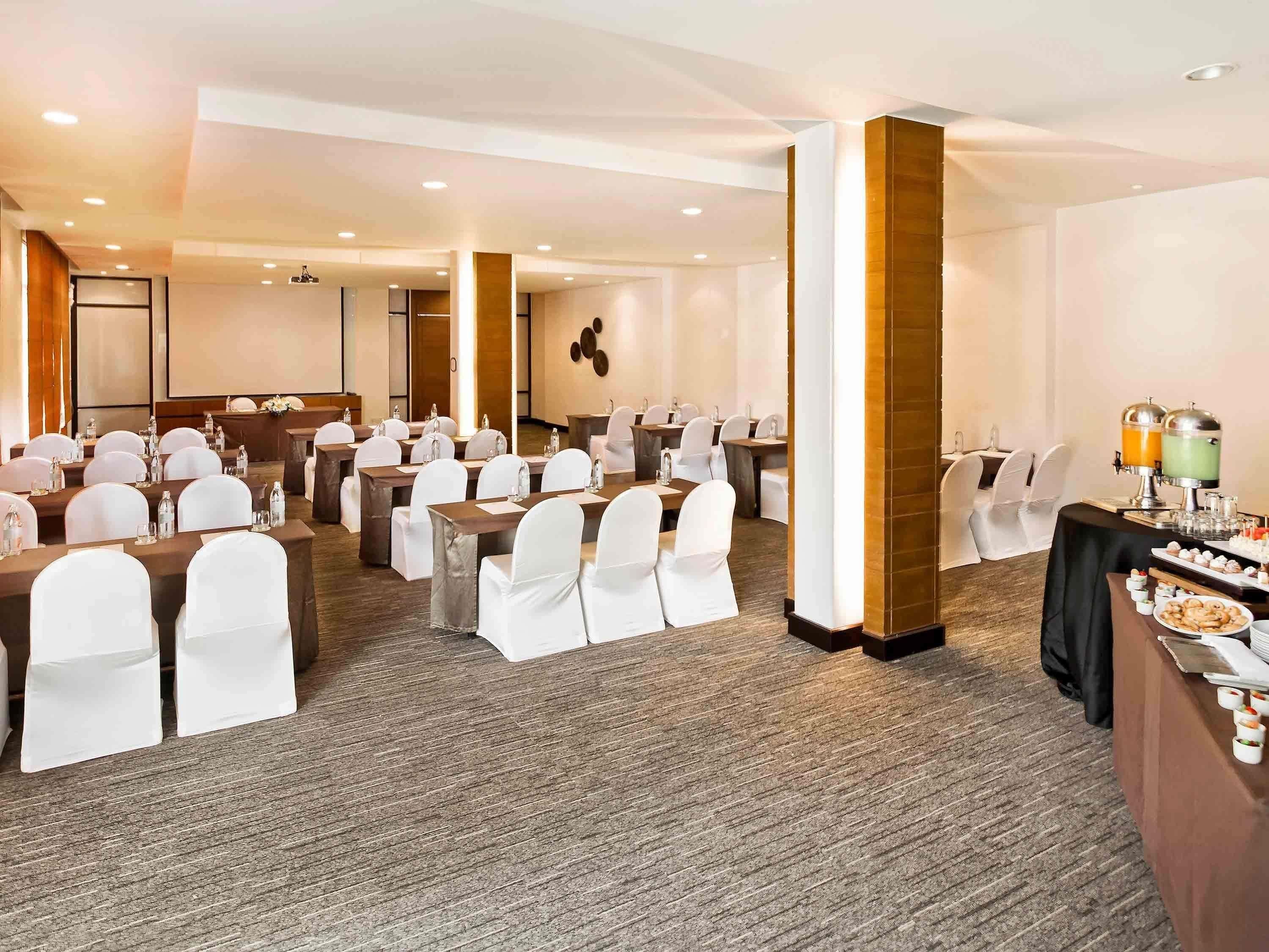 A conference room with tables and chairs, a projector screen, and a buffet area with food and drinks.