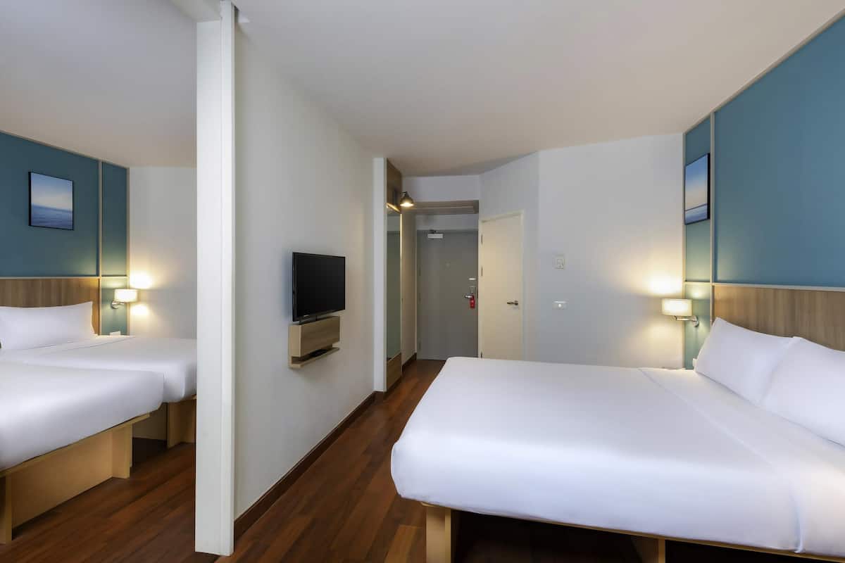 A hotel room with two beds, a TV, and a door leading to a hallway.