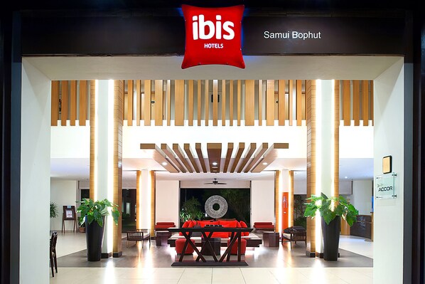 Un hall d’hôtel moderne avec un canapé rouge, des lambris en bois au plafond et des plantes en pot.