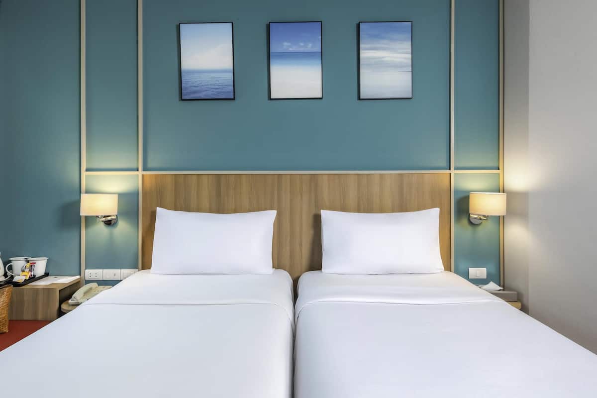 A hotel room with two beds, a wooden headboard, wall-mounted lamps, and three framed pictures above the beds.