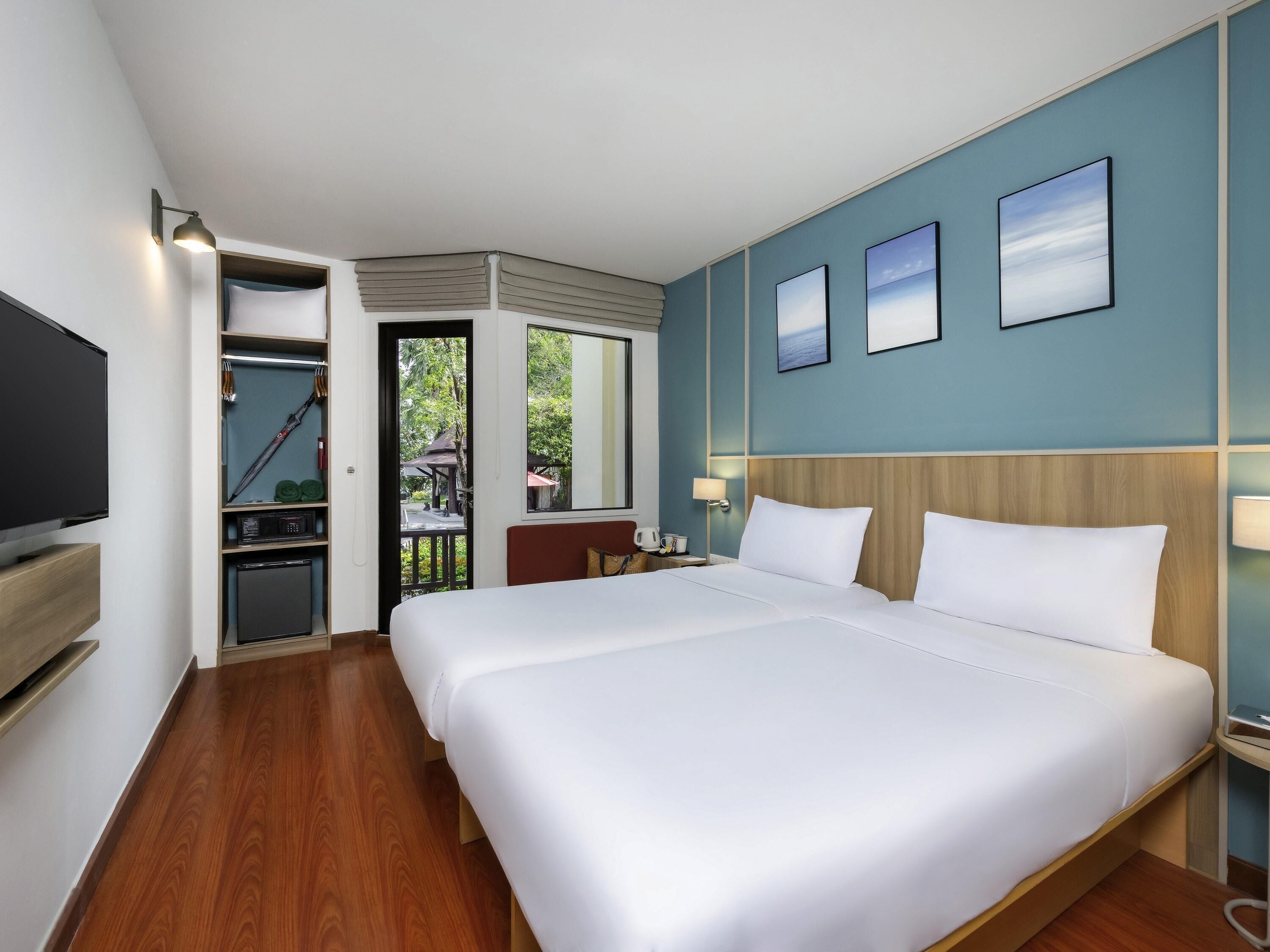 A hotel room with a large bed, a television, a desk with a lamp, and a view of the outdoors.