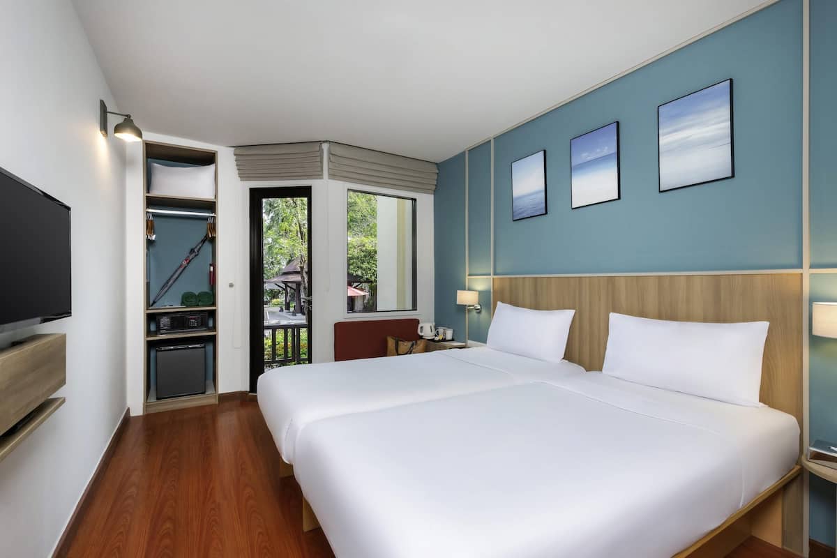 A hotel room with a large bed, a television, a desk with a lamp, and a view of the outdoors.