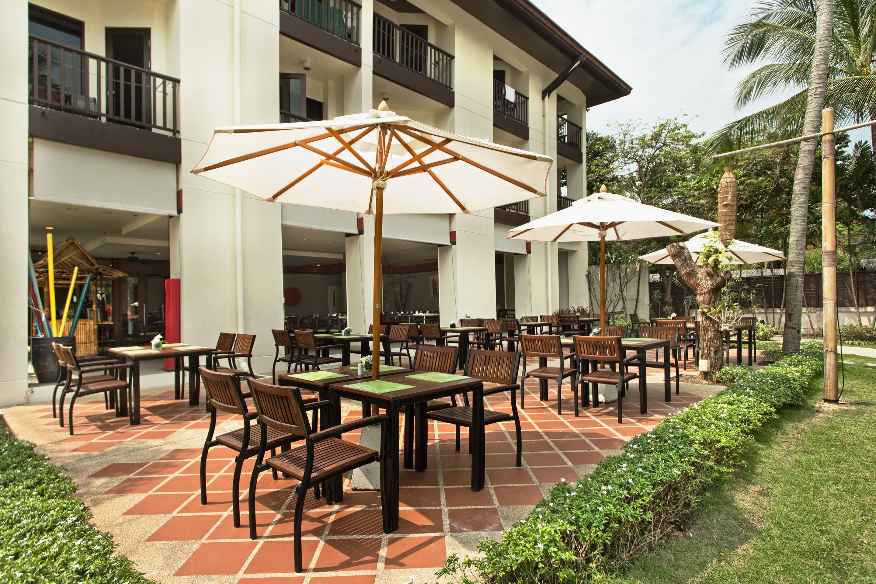 An outdoor patio with multiple tables and chairs, surrounded by a white building with balconies.