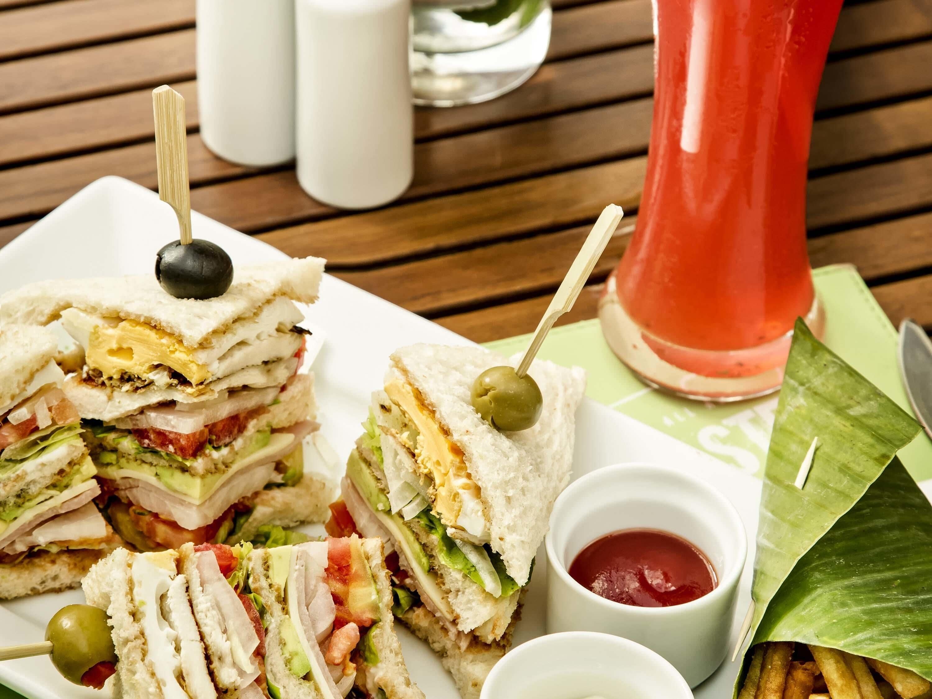 Une assiette de sandwichs aux olives, un verre de boisson rouge et de petits pots de ketchup.