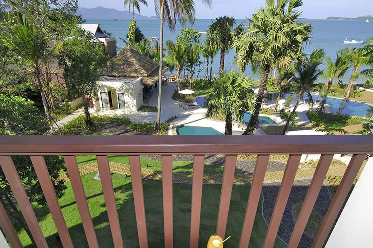 A balcony with a view of a pool, palm trees, and a beach.