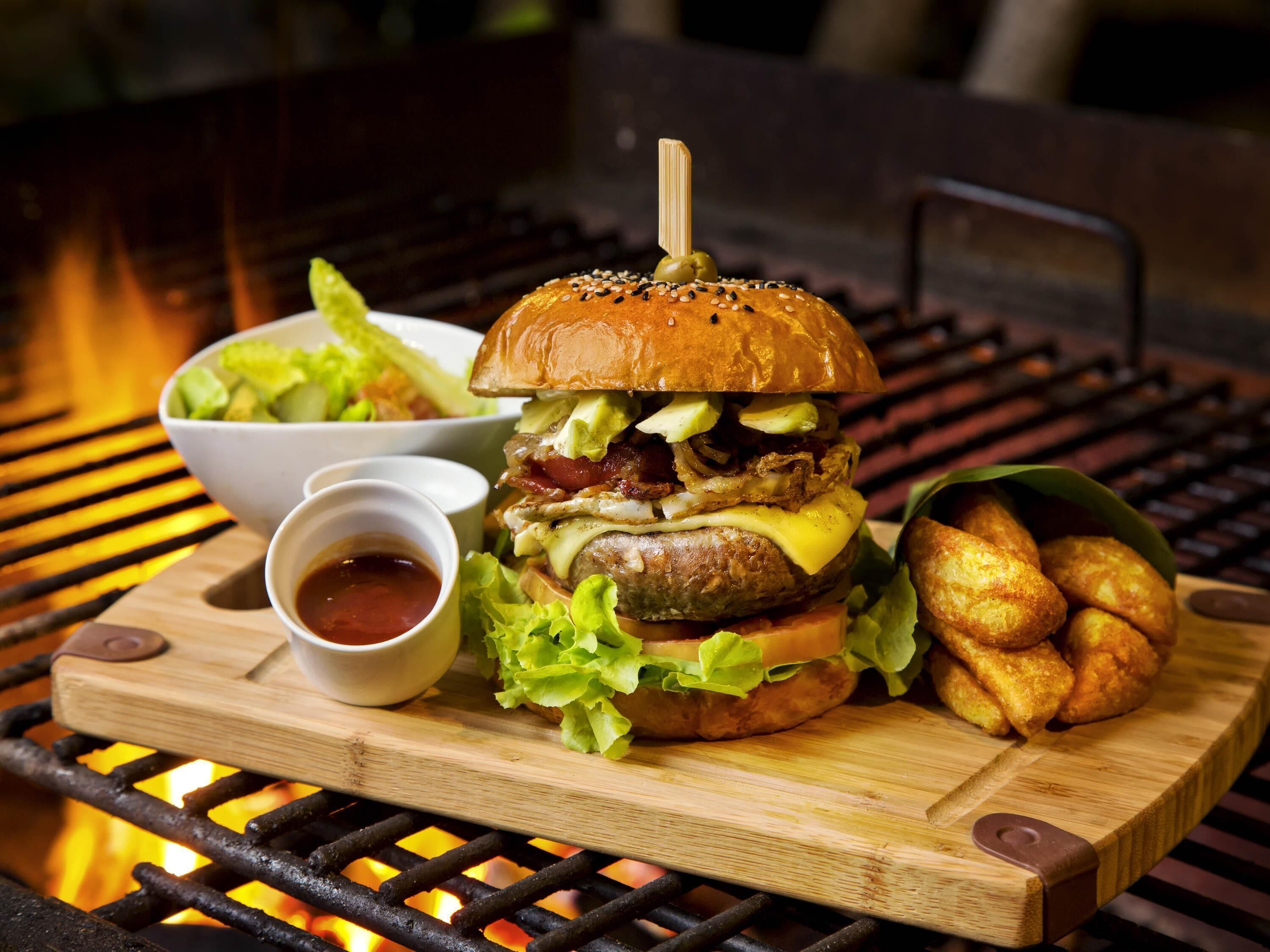A burger with lettuce, cheese, and a bun, served with fries and a side salad on a wooden board.