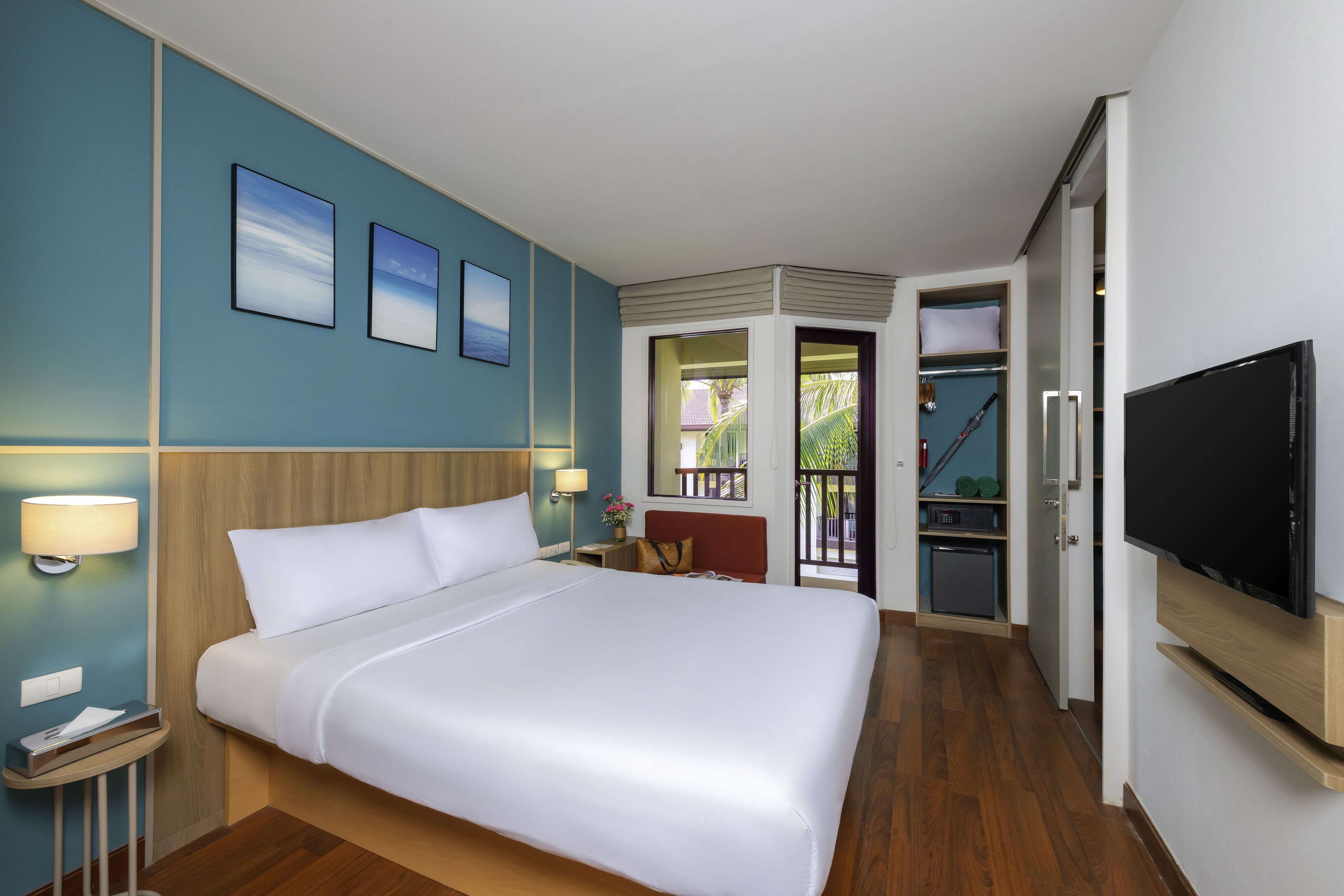 Habitación de hotel con una cama grande, televisión, escritorio con lámpara y vistas al balcón exterior.