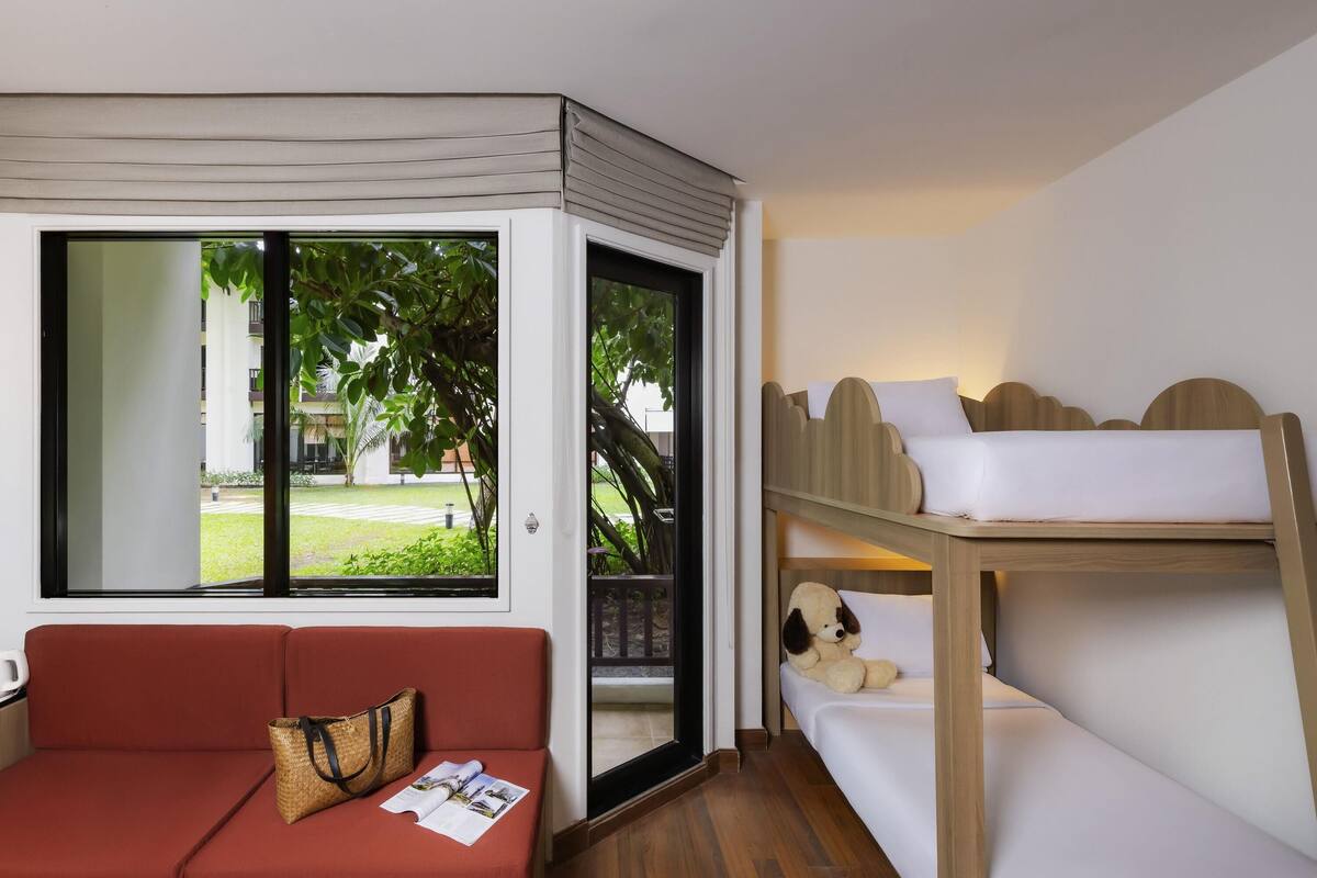 A room with a red sofa, a bunk bed, and a large window offering a view of greenery outside.