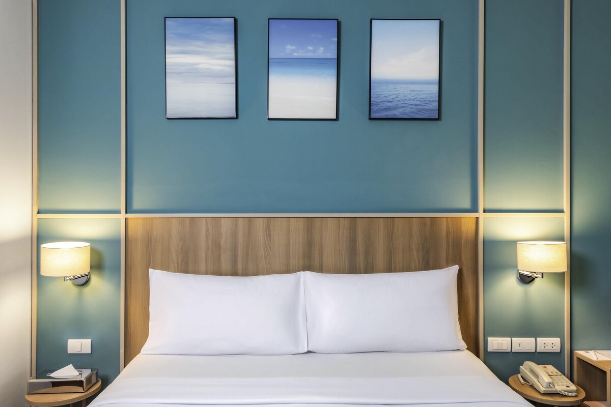 Habitación de hotel con una cama grande, dos lámparas de noche, un cabecero de madera y tres cuadros en la pared.