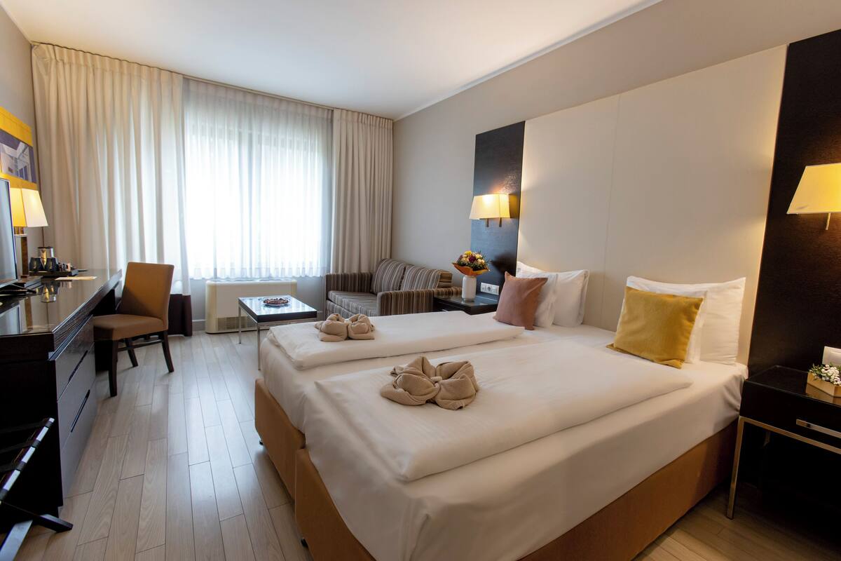 Hotellihuone, jossa on kaksi sänkyä, työpöytä, tuoli, pieni pöytä ja sohva.