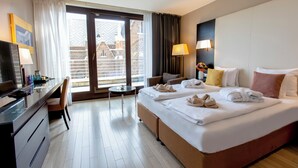A hotel room with a bed, a desk, a chair, a small table, and a balcony with a view. - Lions Garden Hotel (Budapest)